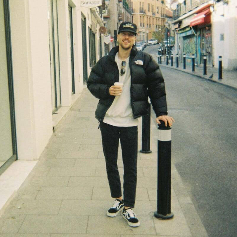 Der Berufswahl-Coach, Simon, steht auf einer Strasse mit einem Kaffee in der Hand und lächelt in die Kamera